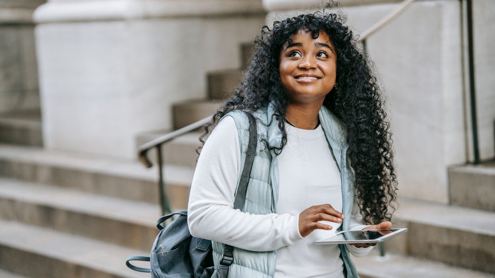 Estudante sorridente com tablet nas escadas do campus, a escolher o curso com mais hipóteses de entrar na UP