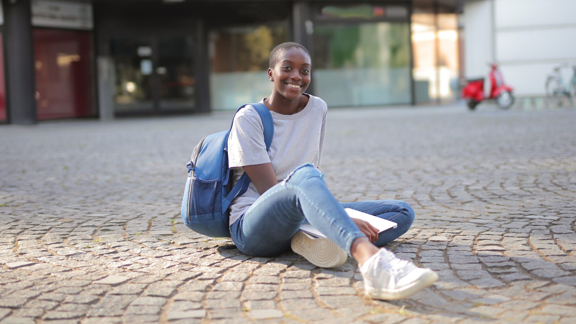 Estudante sorridente com mochila e portátil, sentada na rua, a preparar a candidatura ao IFP 2027