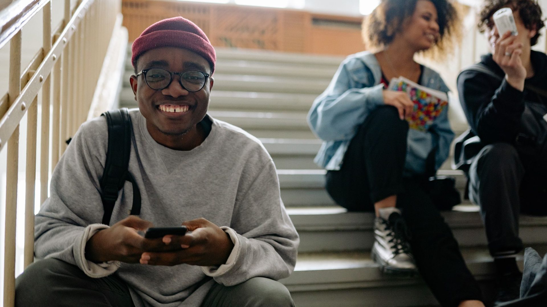 Estudante sorridente com telemóvel nas escadas do campus universitário, a consultar a candidatura à UJC