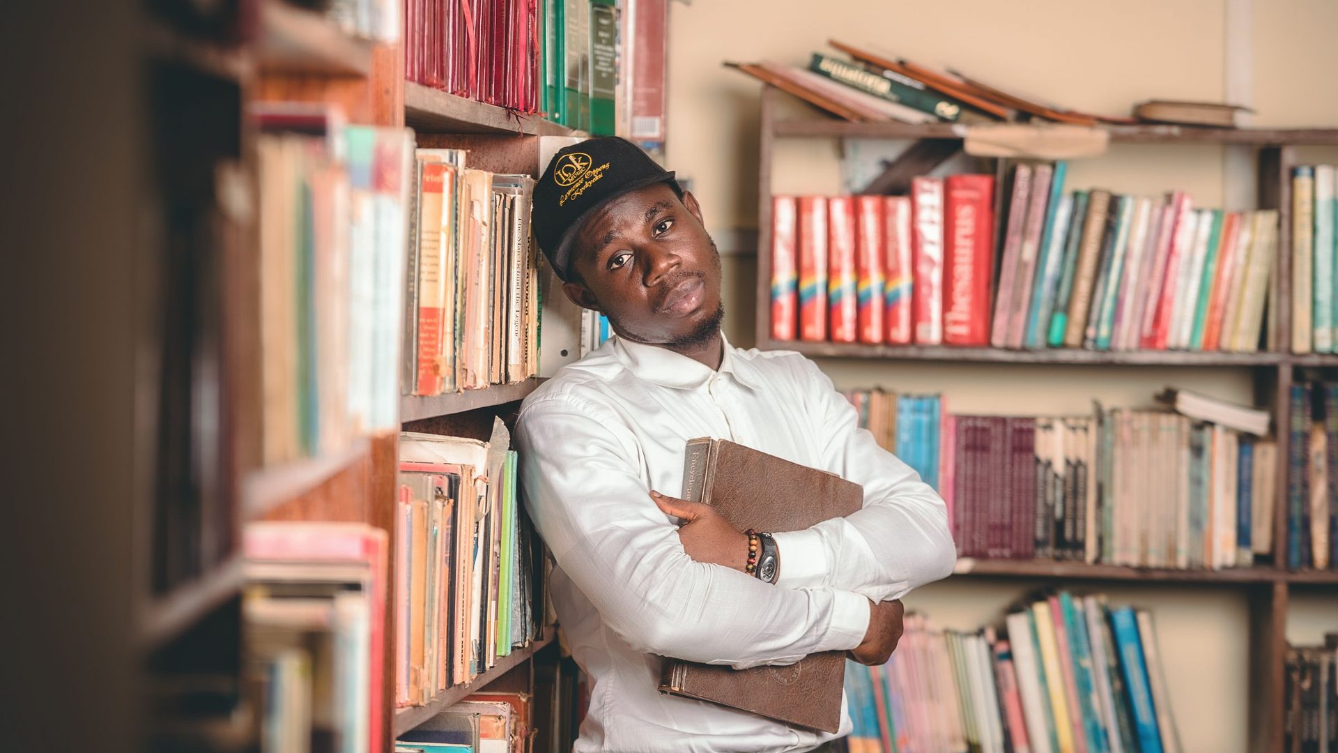 Jovem numa biblioteca com um livro na mão, rodeado de estantes cheias de livros
