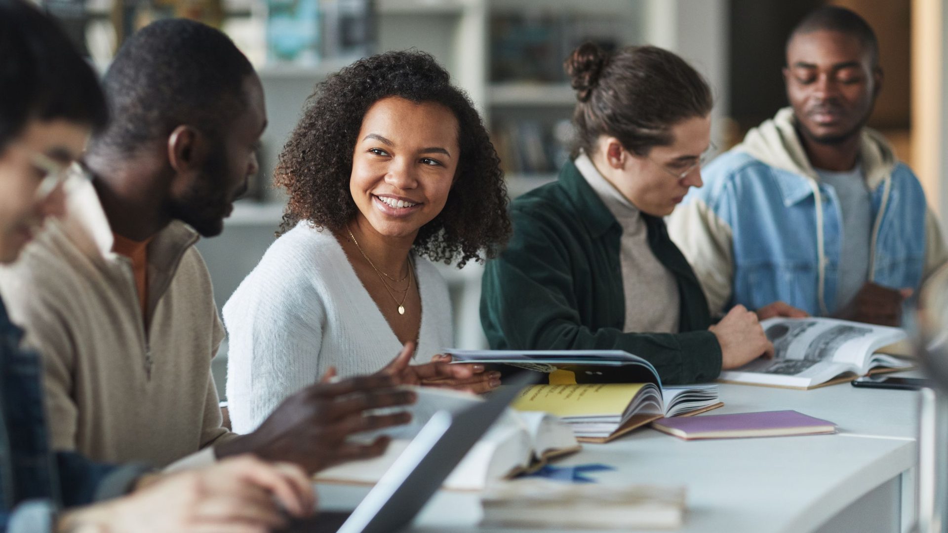 Grupo de estudantes sorridentes a estudar juntos à volta de uma mesa com livros e cadernos