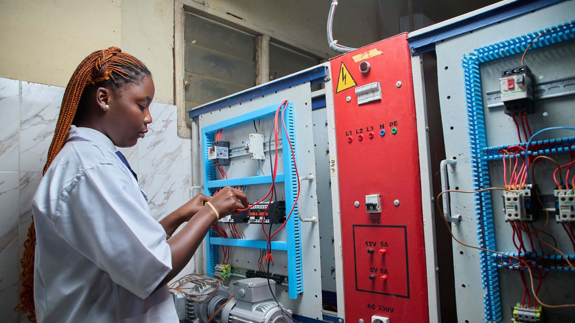 Jovem técnica de bata branca a ligar cabos num painel eléctrico de formação