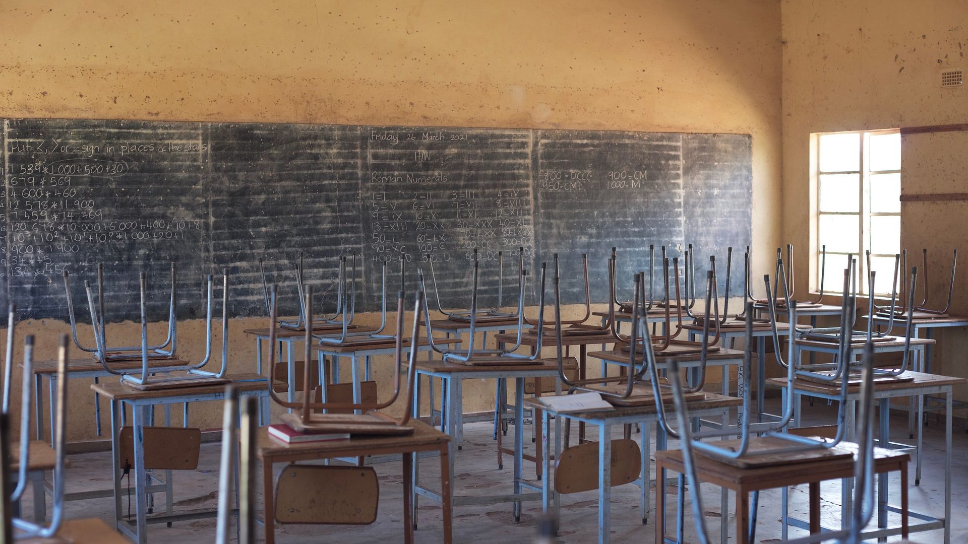 Sala de aula vazia de uma escola rural, com carteiras de madeira alinhadas e um quadro preto ao fundo