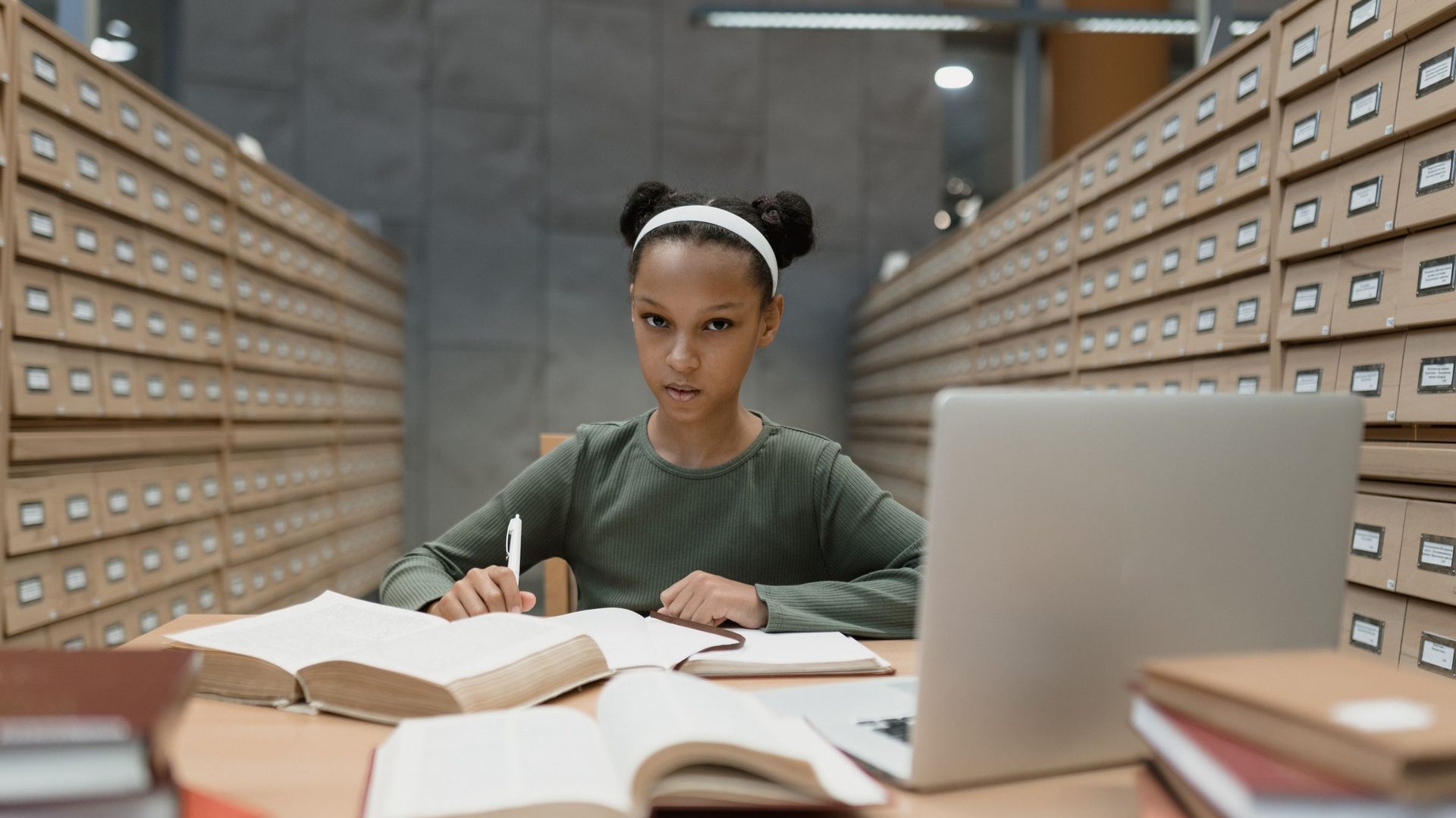 Jovem concentrada a estudar numa mesa de biblioteca, com livros e um portátil