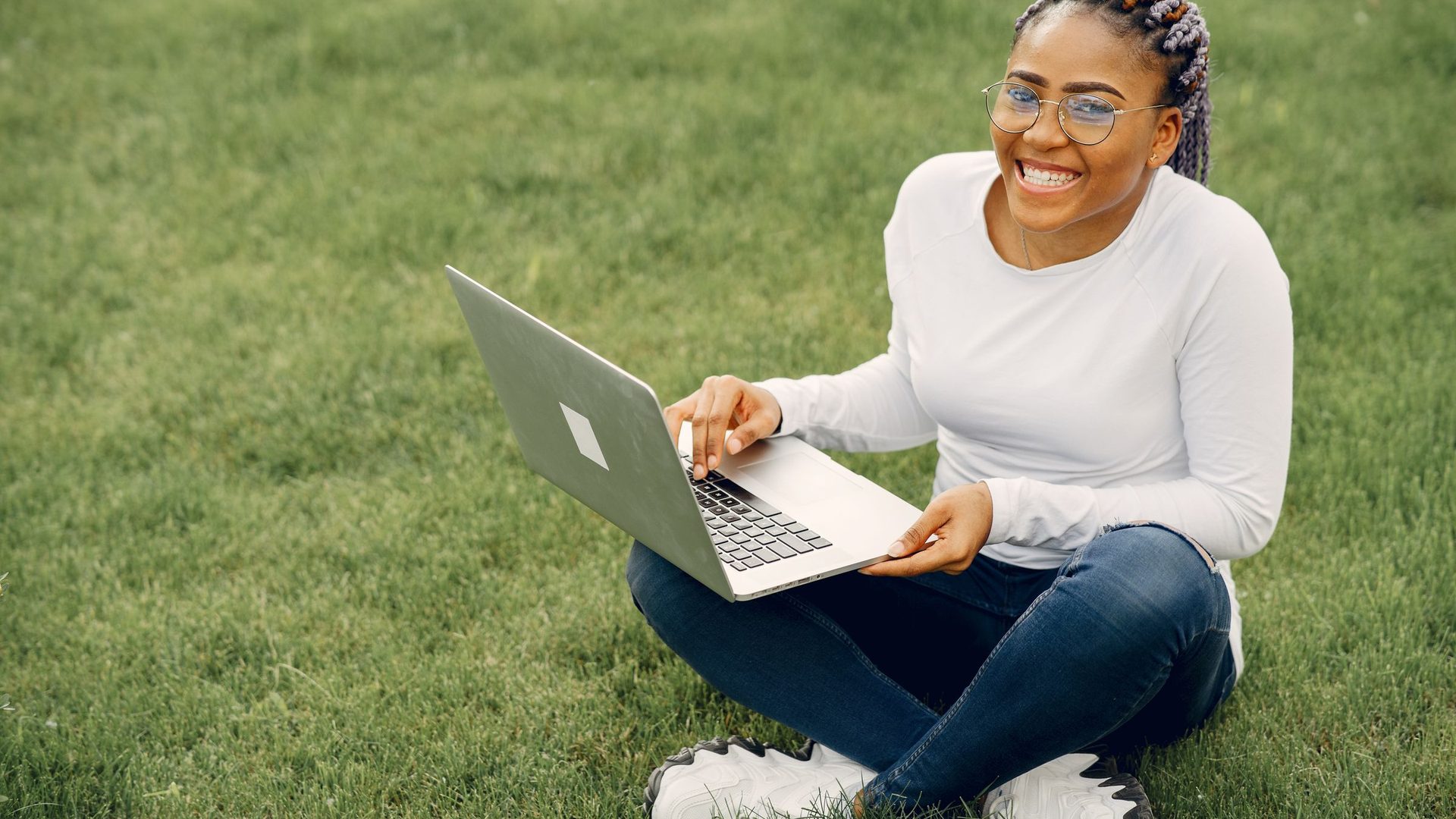 Estudante sorridente sentada na relva com o portátil, a fazer a pré-inscrição online na UP